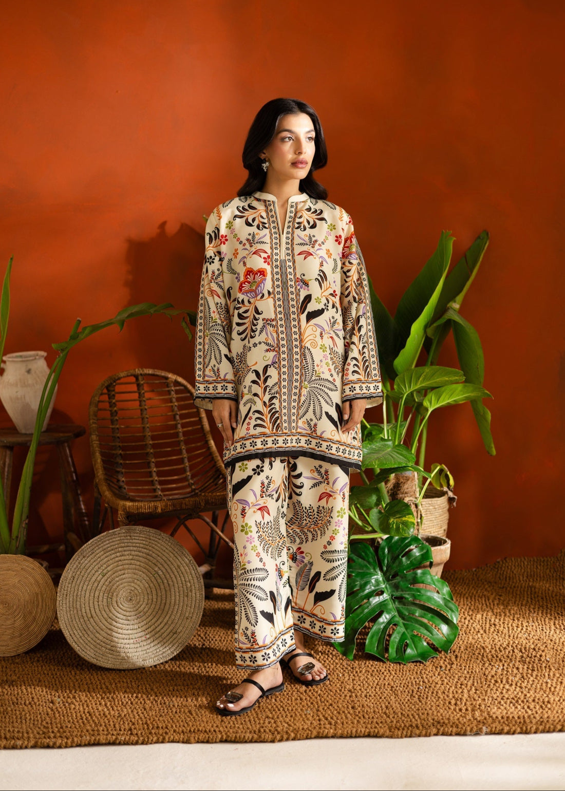 Woman in a patterned Printed co-ord set standing in a room with plants and a red wall.