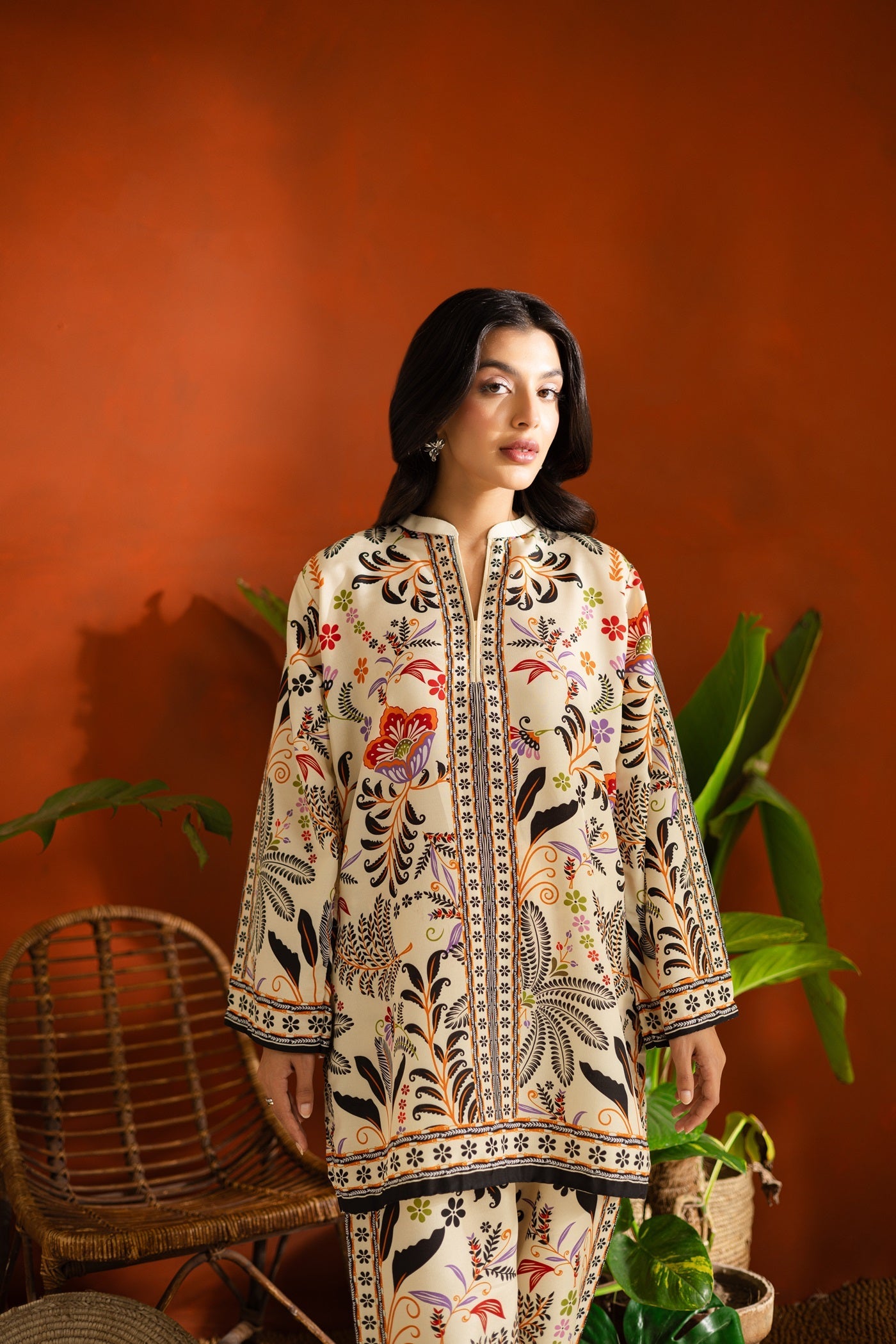 Woman wearing a Flower and plants patterned Printed outfit against an orange wall with plants.