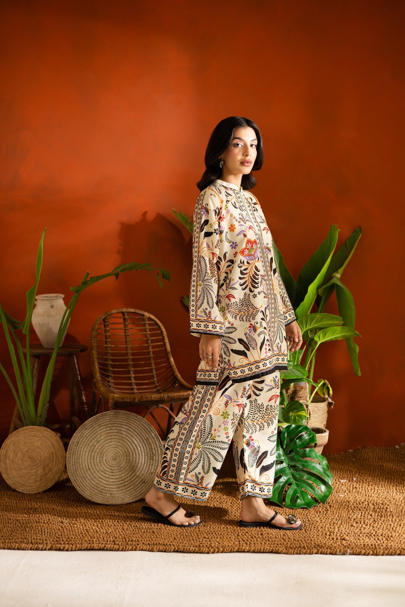 Woman in a patterned Floral Printed Co-ord set standing in front of an orange wall with plants.