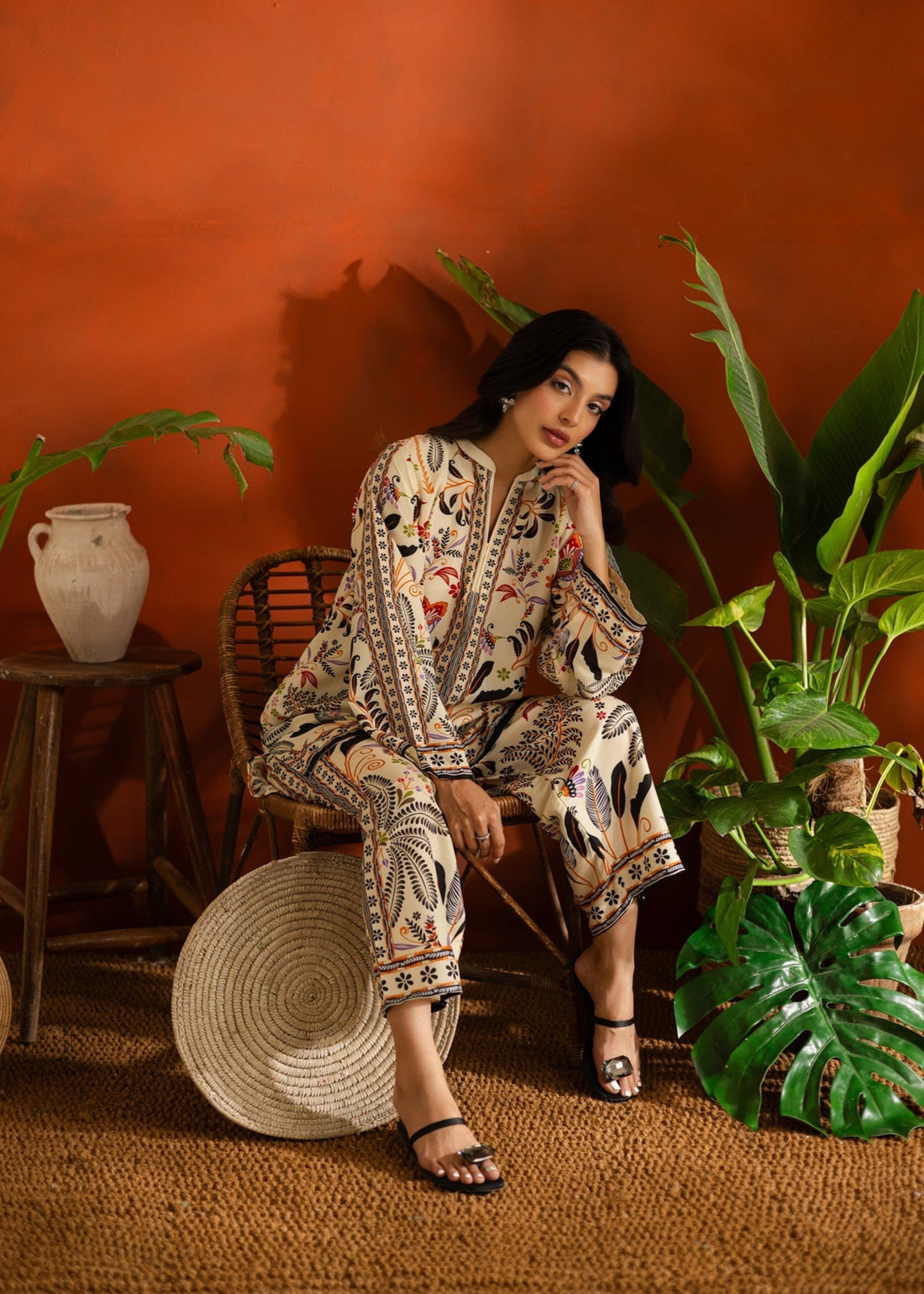 Woman in a patterned Printed co-ord set standing in a room with plants and a red wall.