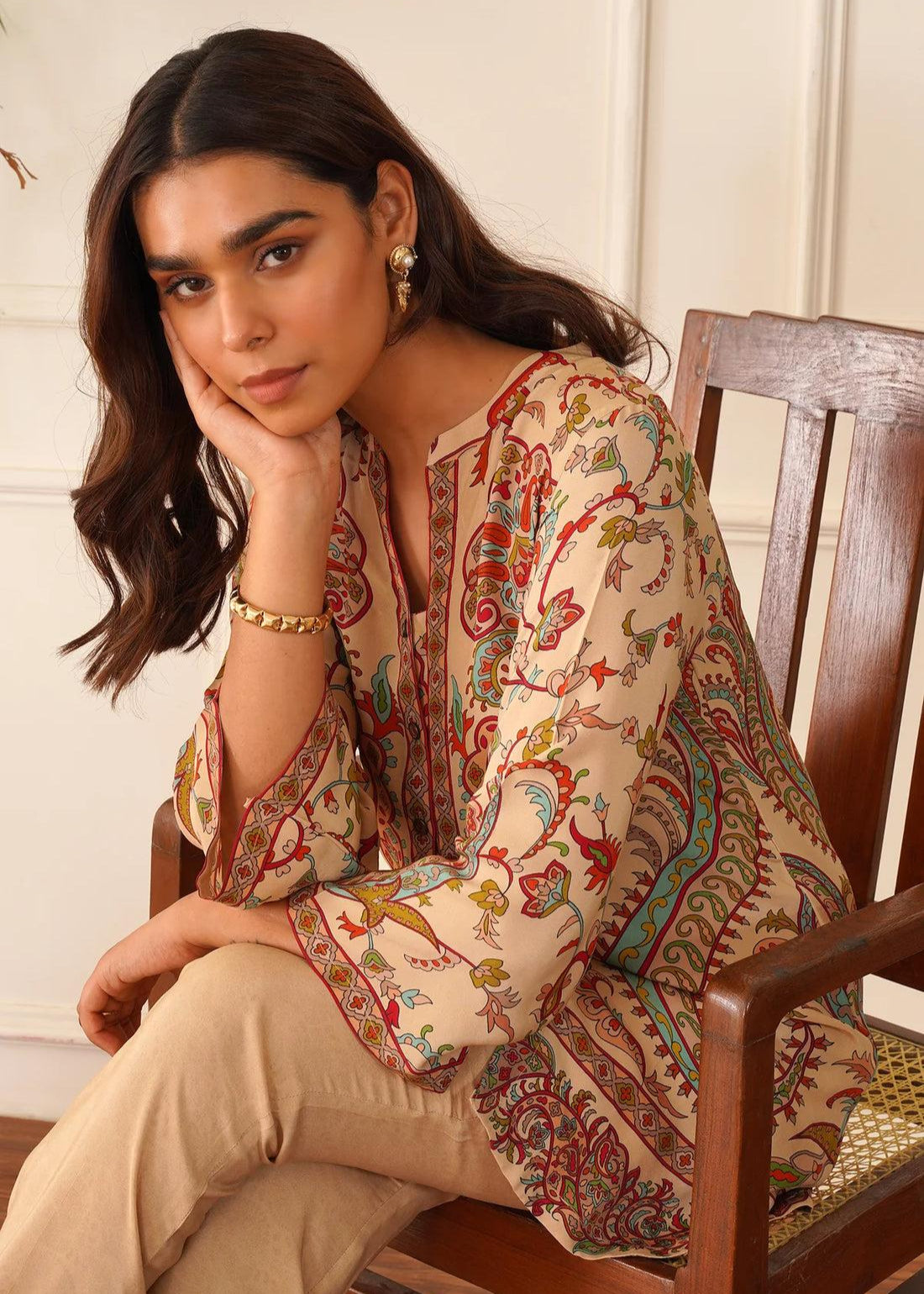 Woman wearing a patterned top sitting on a wooden chair.